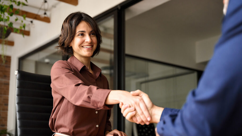 Happy young business woman bank manager handshaking client at meeting. Smiling female hr hiring recruit at job interview, insurance agent, lawyer making contract deal at work with business handshake.